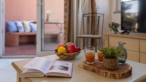 Une pièce dans laquelle se trouve une table, dressée avec un livre, un panier de fruits, des verres de jus d’orange et une petite plante.