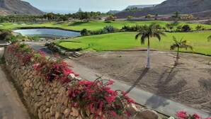 Un parcours de golf agrémenté d’un étang, de palmiers et d’un mur de pierre orné de fleurs roses.