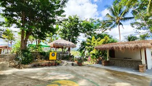 Un complexe hôtelier tropical doté de bâtiments à toits de chaume, de plantes en pot et d’un panneau indiquant la présence d’un jeu de fléchettes.