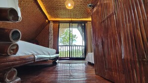 Une pièce avec un plafond en pente, des poutres en bois, un lit avec une literie blanche et une vue sur la verdure à l’extérieur.