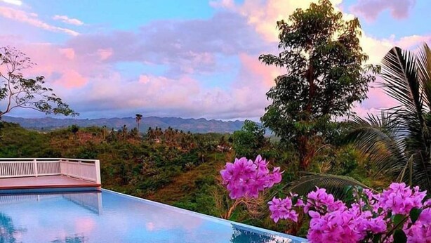 Une piscine à l’eau cristalline, entourée d’une végétation luxuriante et de fleurs roses.