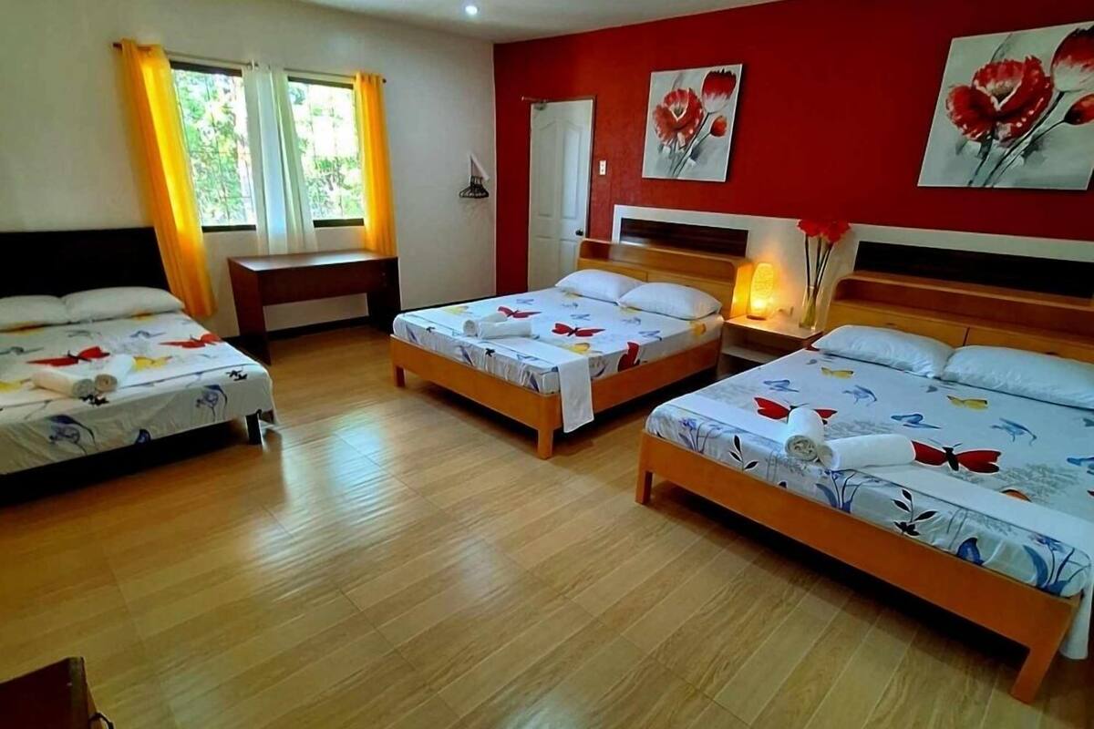 A hotel room with three beds, wooden flooring, and red walls.