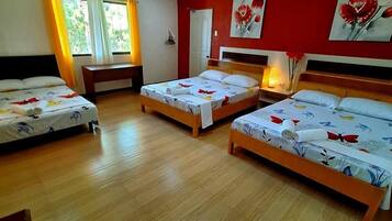 Habitación de hotel con tres camas, piso de madera y paredes rojas.