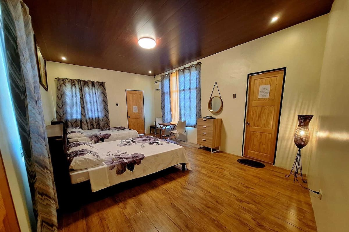 A bedroom with two beds, a dresser, a desk, and a lamp.
