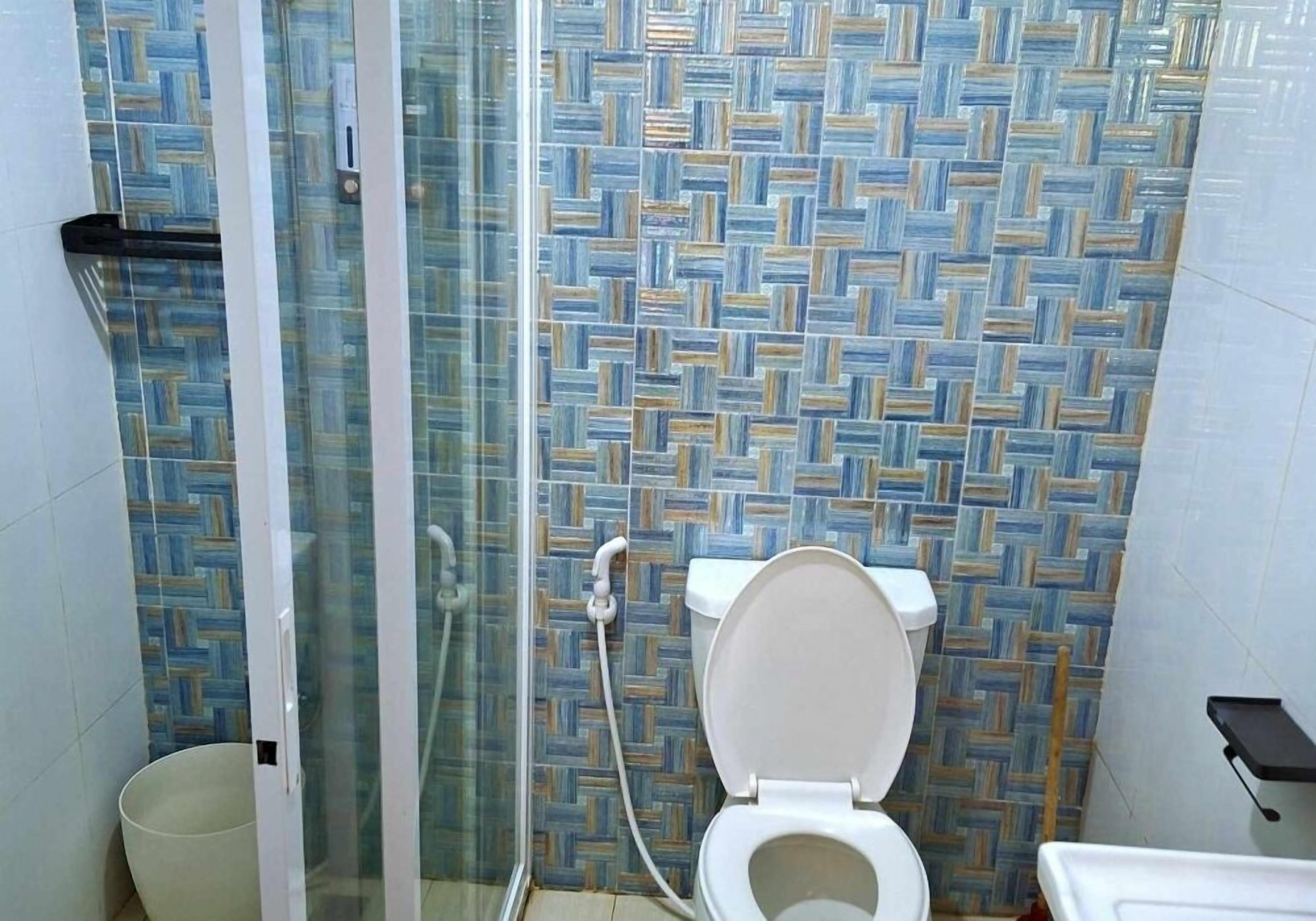 A bathroom with a patterned tile wall, a toilet, a glass shower enclosure, and a small shelf.