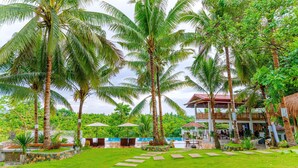 Un complexe hôtelier tropical doté de palmiers, d’une piscine et d’un bâtiment à deux étages surmonté d’un toit rouge.