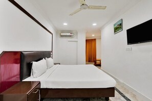 Quarto de hotel com cama, ventoinha no teto, aparelho de ar condicionado, televisão e quadro na parede.