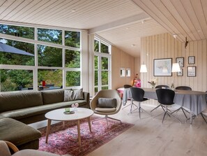 Een ruime woonkamer met een groot raam, een bank, een salontafel en een eethoek met stoelen en een tafel.