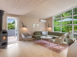 Un salon chaleureux avec une cheminée, un canapé, une table basse et une grande fenêtre donnant sur un paysage verdoyant.