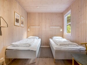 A room with two single beds, wooden walls, a window, and wall-mounted lights.