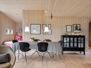 A modern dining area with a wooden ceiling, a dining table with chairs, and a black cabinet with glass doors.
