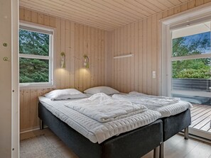 Een slaapkamer met een bed, twee wandlampen en een raam met uitzicht op bomen.