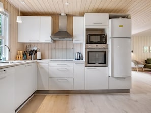 Une cuisine moderne avec des meubles blancs, un four encastré, un four à micro-ondes et un grand réfrigérateur.