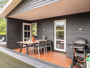 A covered outdoor patio with a table and chairs, a grill, and a sliding glass door.