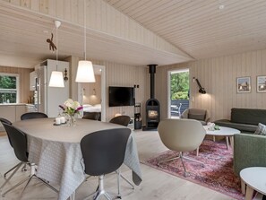 Un intérieur moderne comprenant un coin repas, une cuisine et un espace de vie, avec des murs en bois, une cheminée et des meubles contemporains.