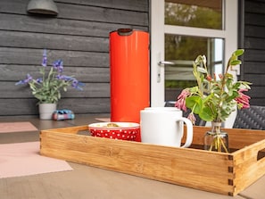 A wooden tray with a white mug, a red mug with white polka dots, and a red container on a wooden table.