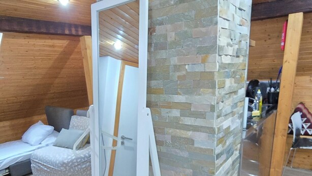 Quarto com parede de pedra, uma cama e uma porta branca com espelho.