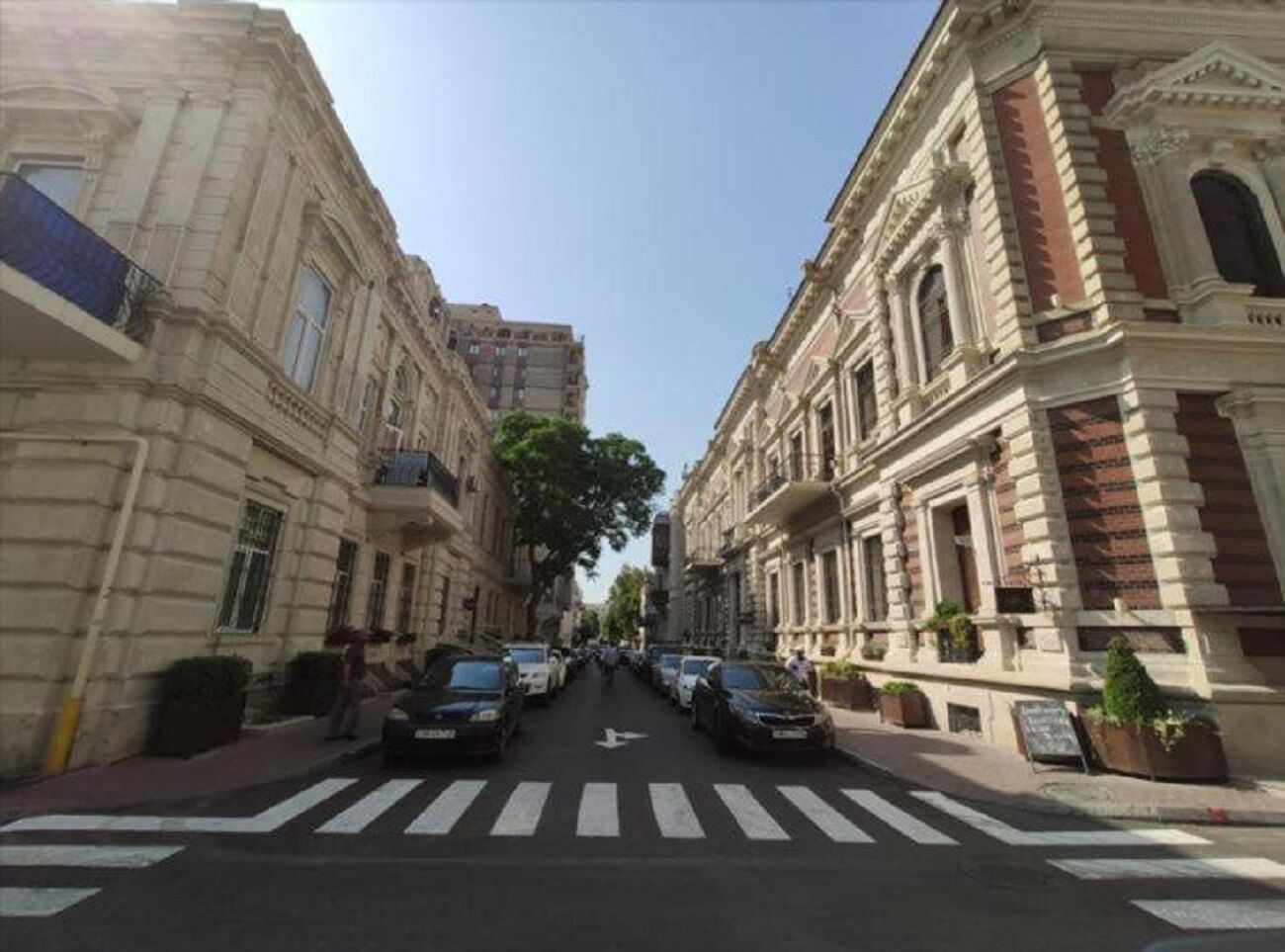Vista de una calle en la ciudad, con edificios a ambos lados, un paso de cebra y coches aparcados.