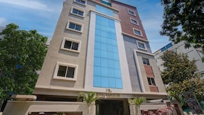 A multi-story hotel with a prominent blue glass facade, a sign reading "VR Royal Signature," and a modern architectural design. - iROOMZ J3 Group of Hotels (Hyderabad)