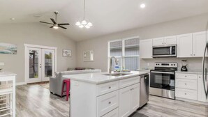 A modern kitchen with white cabinetry, a central island, stainless steel appliances, and a ceiling fan. - Sea Glass Paradise Pet-Friendly 5 Mins From Beach! (Pensacola)