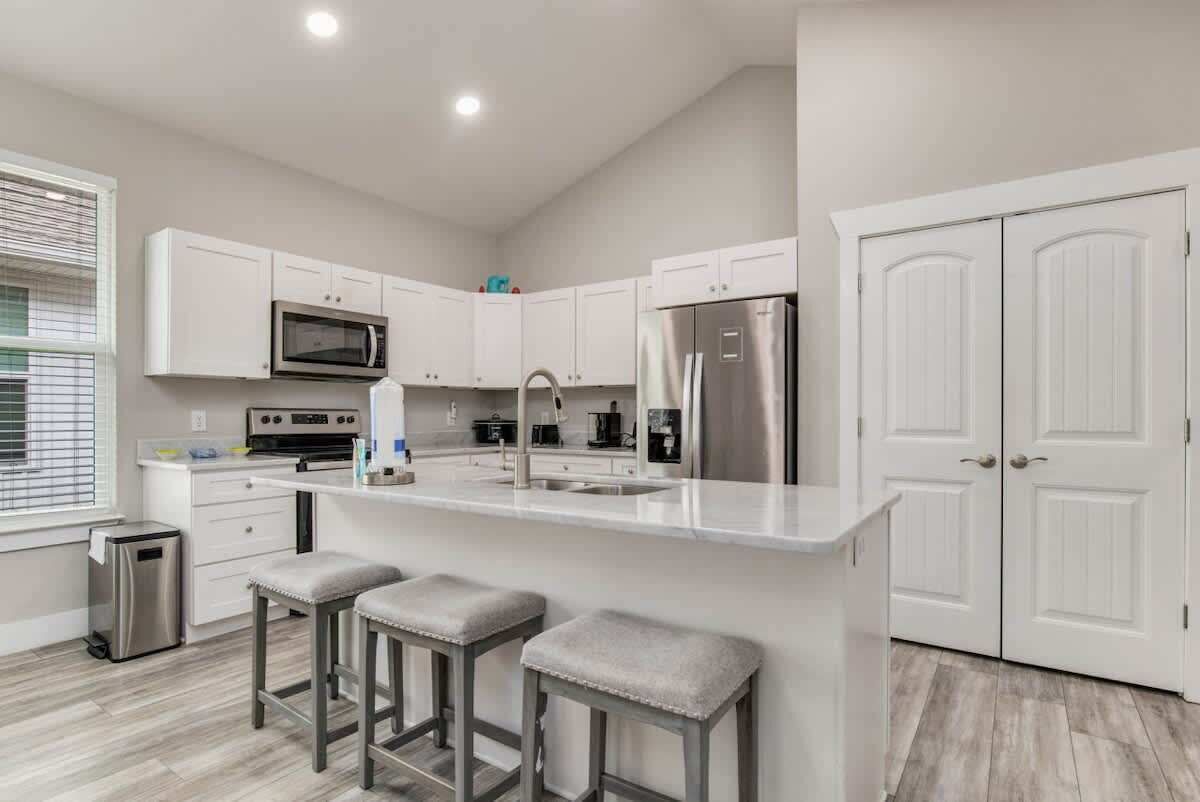 A modern kitchen with white cabinetry, stainless steel appliances, and a central island with stools.