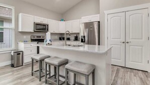 A modern kitchen with white cabinetry, stainless steel appliances, and a central island with stools. - Sea Glass Paradise Pet-Friendly 5 Mins From Beach! (Pensacola)