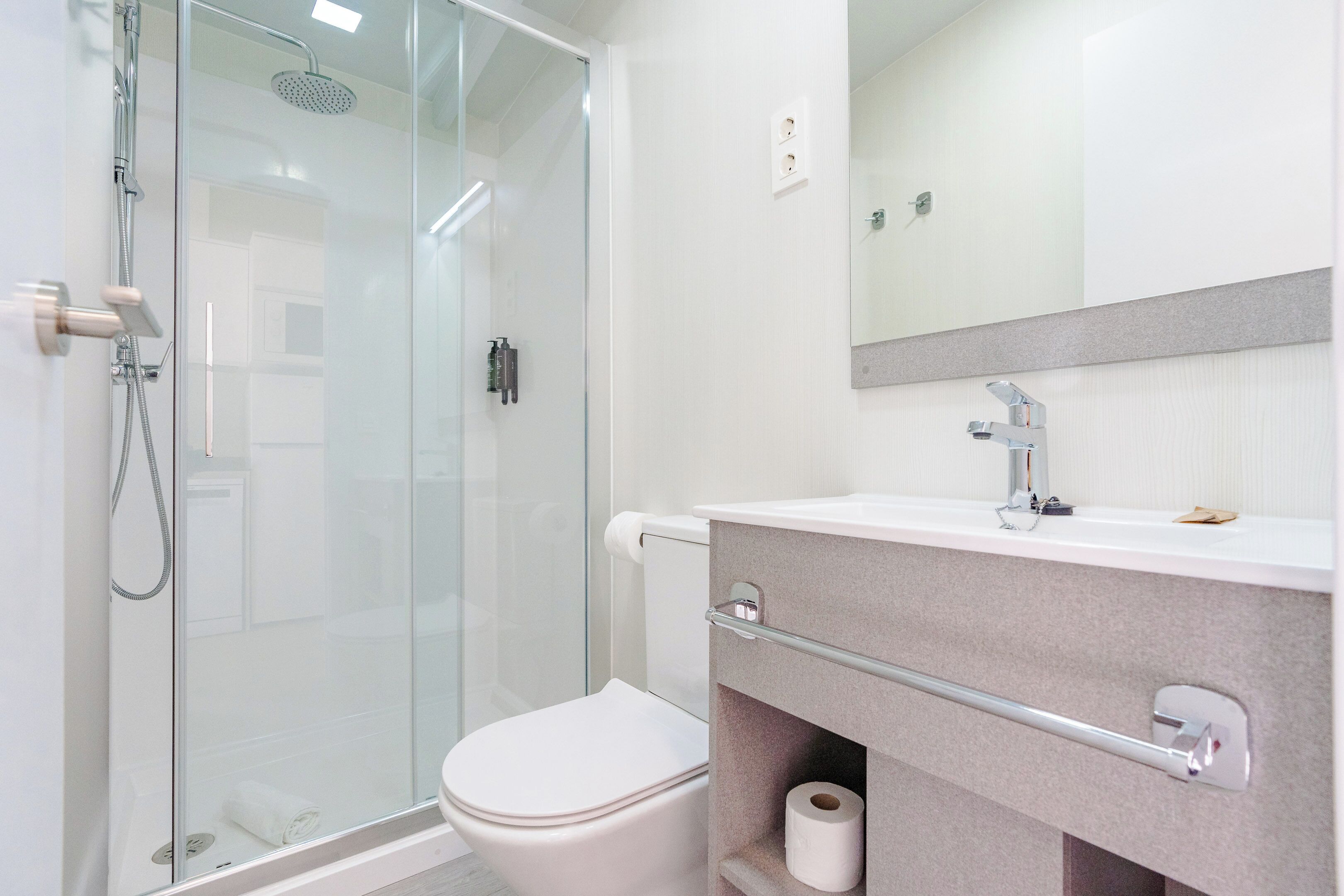 Un baño moderno con ducha de vidrio, inodoro, tocador con espejo y un perchero para toallas.
