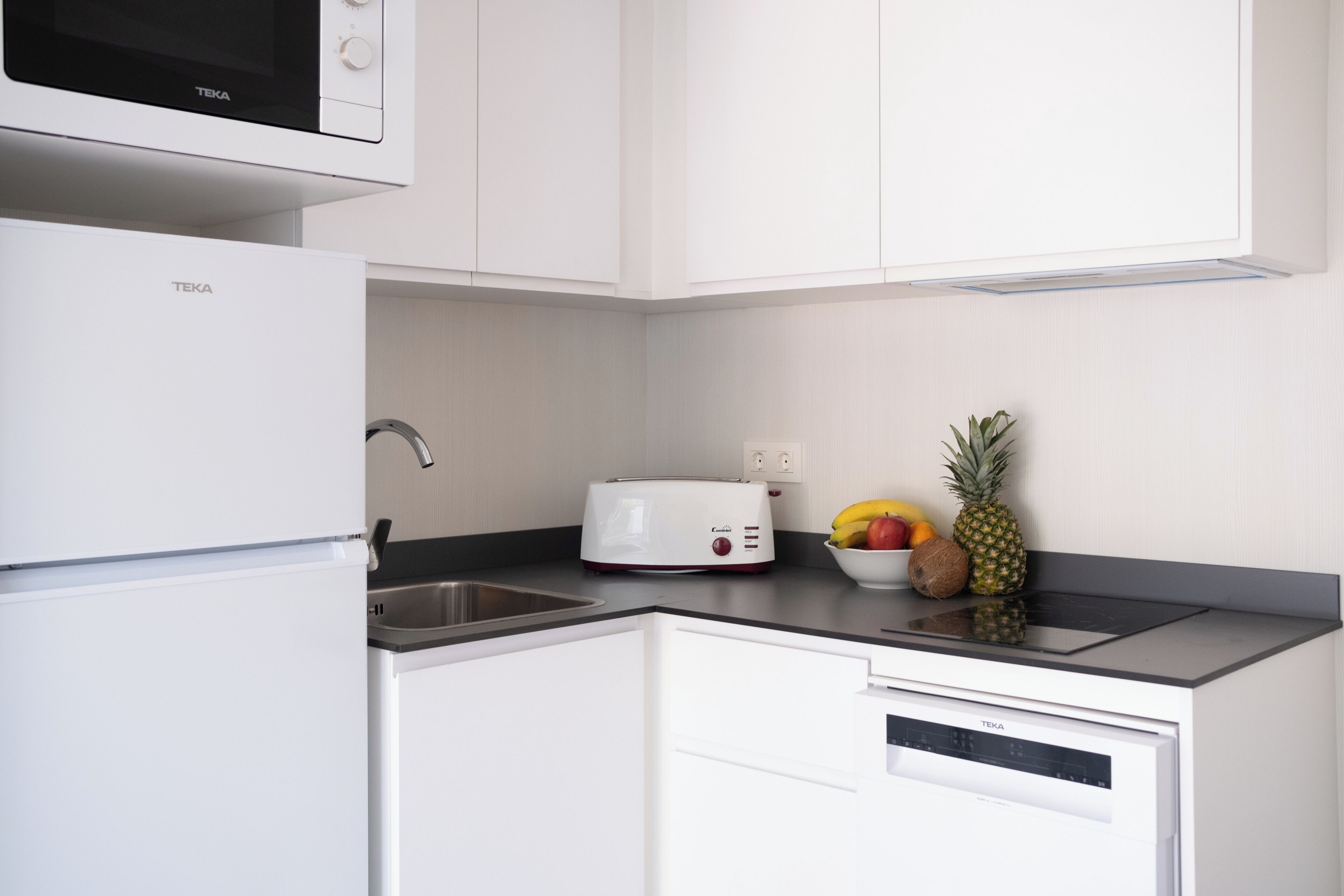 A kitchen with white cabinetry, a microwave, a toaster, and a bowl of fruit on the counter.