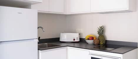 A kitchen with white cabinetry, a microwave, a toaster, and a bowl of fruit on the counter.