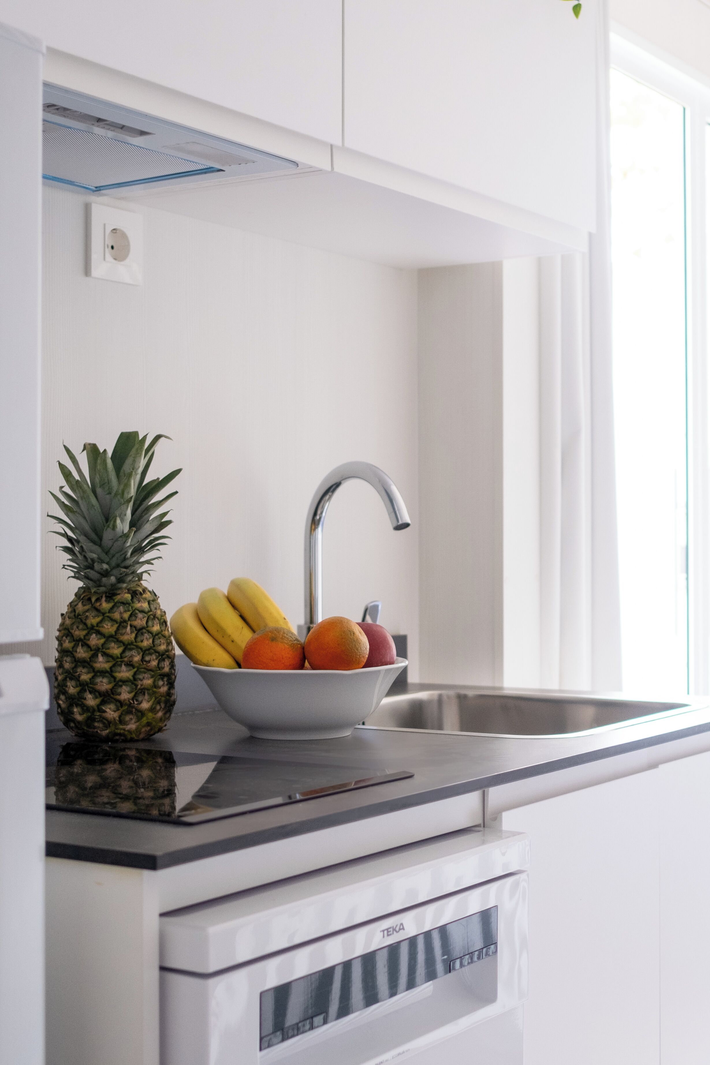 Une cuisine équipée d’un évier en acier inoxydable, d’un saladier rempli de fruits et d’un appareil de la marque TEKA.