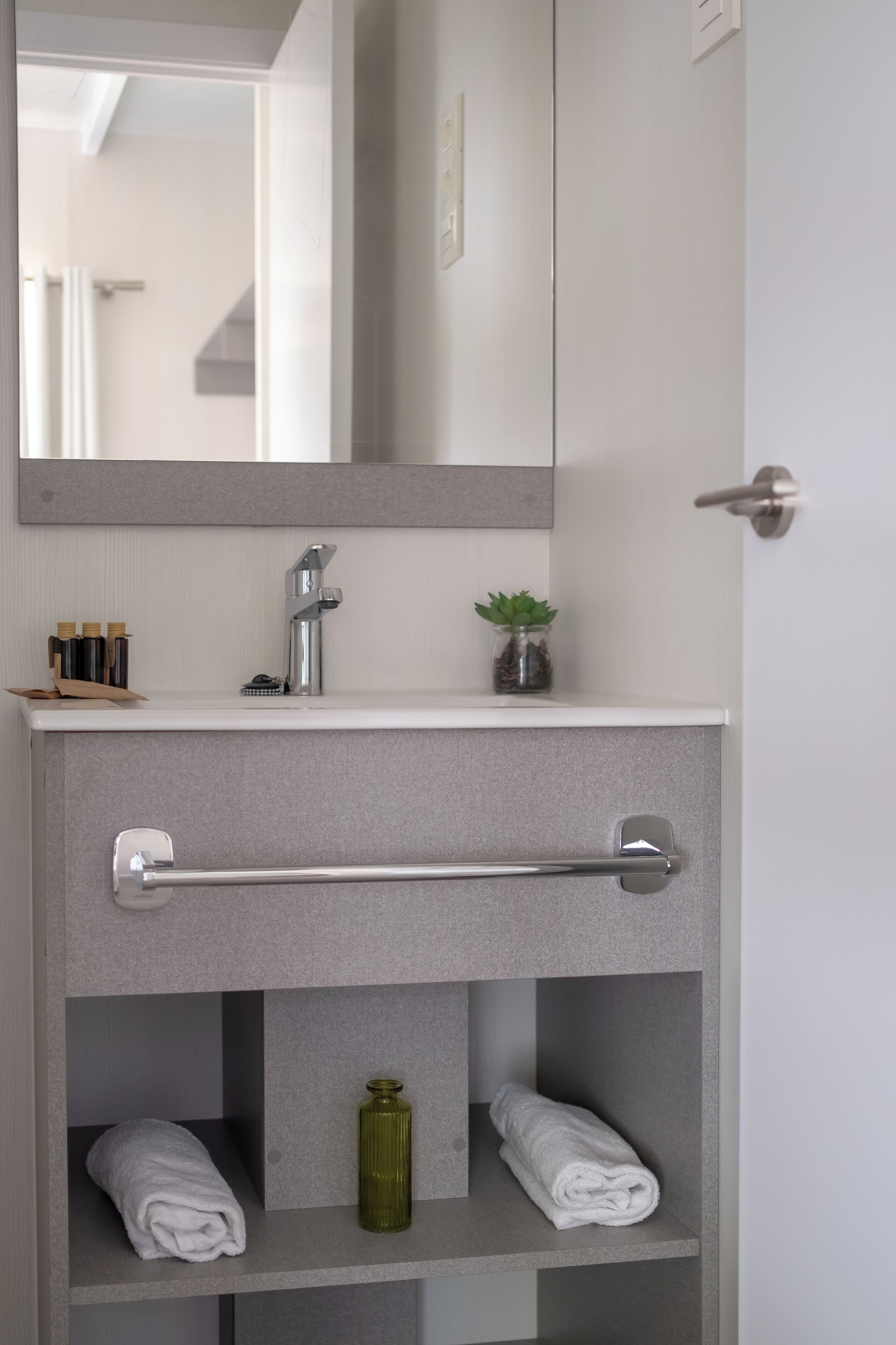 Un baño con un lavamanos blanco, un perchero, un florero de vidrio y un espejo.