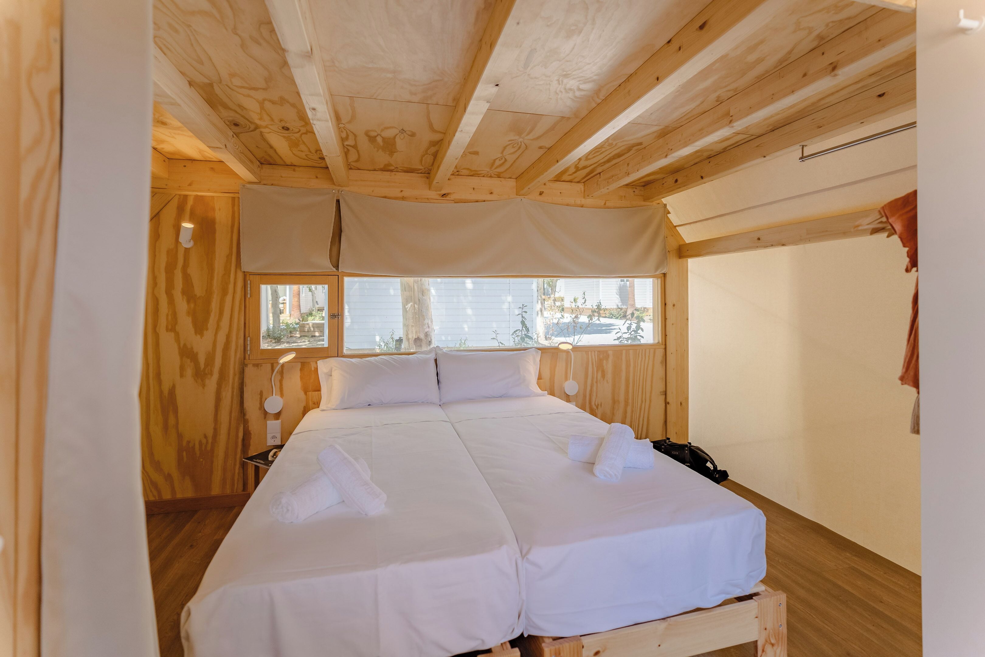 Habitación de cabaña de madera con una cama, una mesita de noche y una ventana con vistas al exterior.