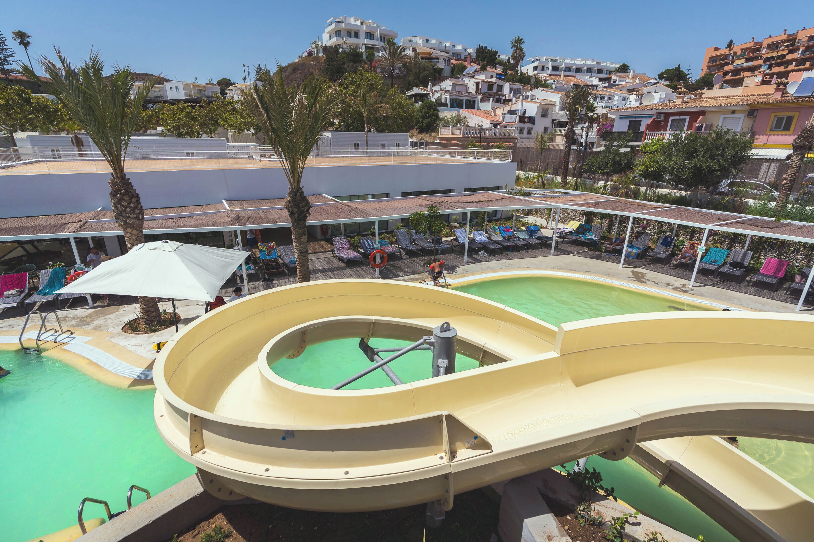 Un tobogán de agua en un resort con piscina, sillas de descanso y vistas de los edificios circundantes.