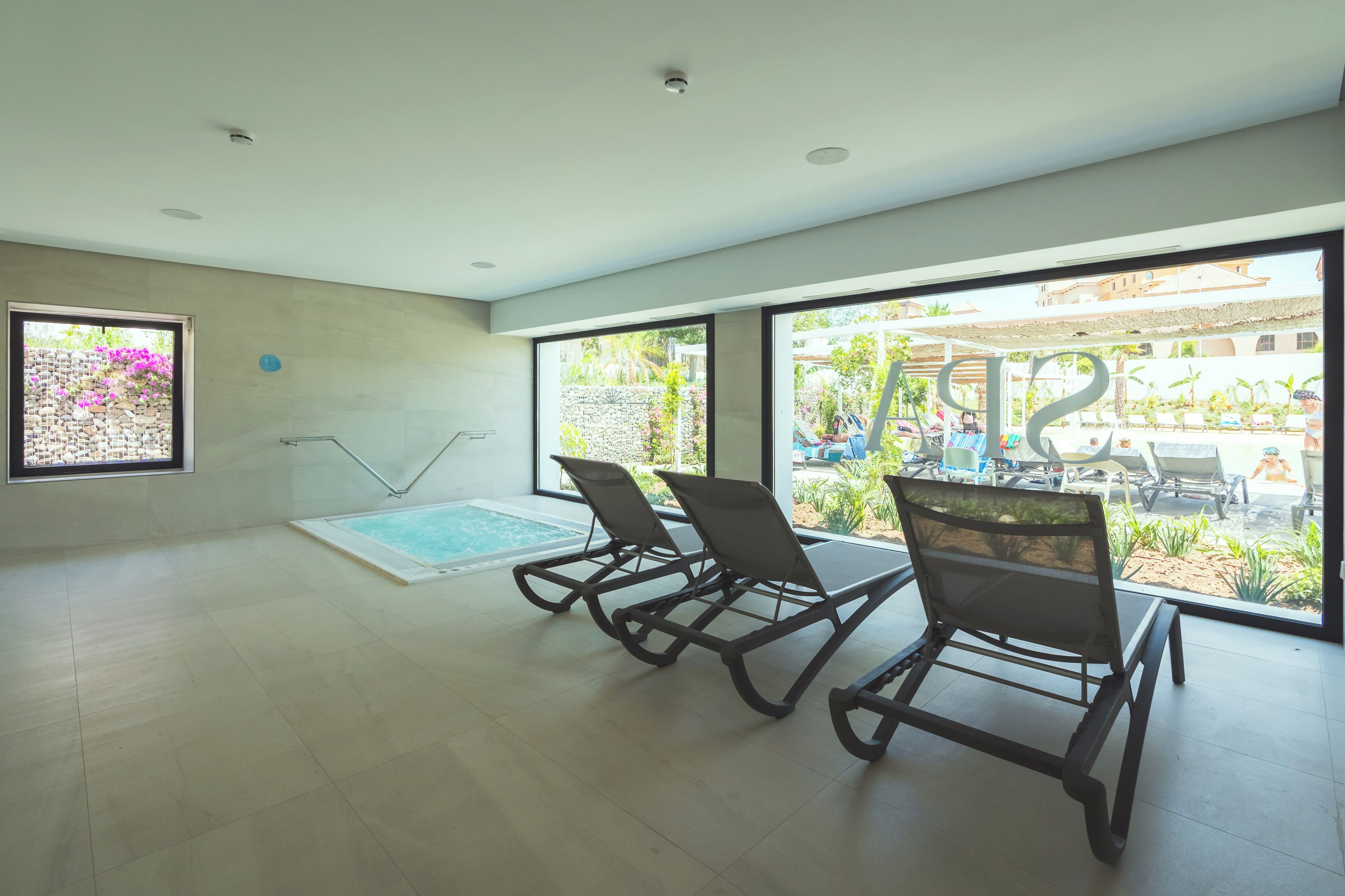 A spacious indoor area with a pool, large windows, and a view of an outdoor pool area.