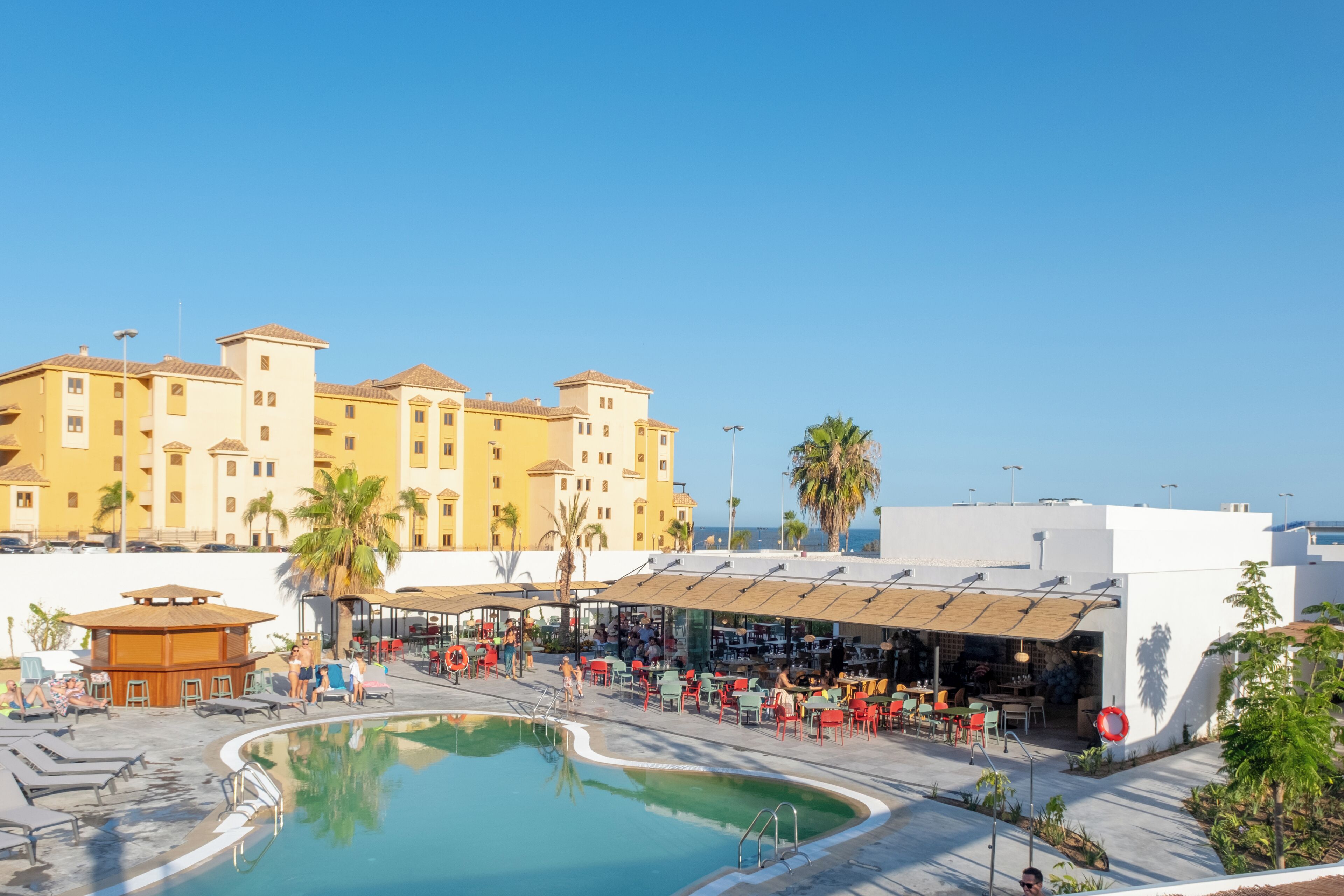 A hotel with a pool area, outdoor seating, and a large building in the background.