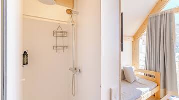 A wooden cabin with a shower, a bed with a view, and a window with curtains.