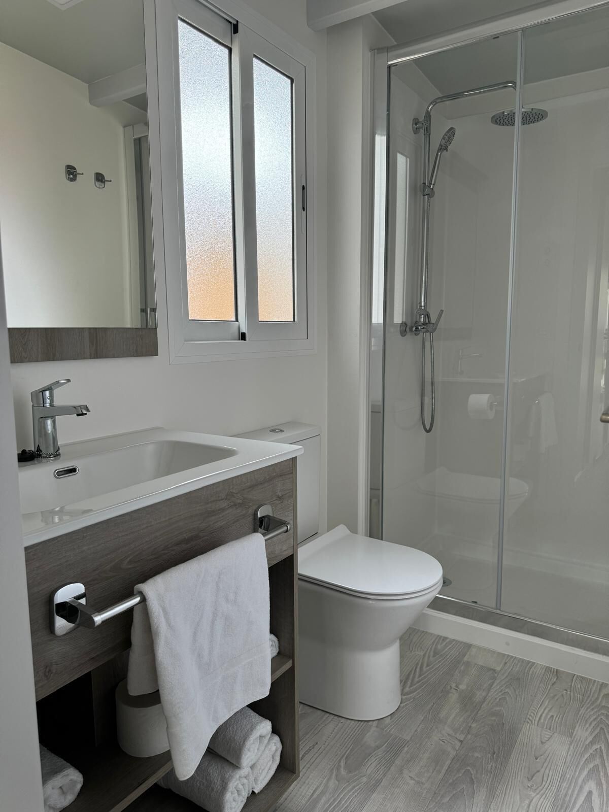 Een moderne badkamer met een douchecabine van glas, een witte wastafel en een toilet.