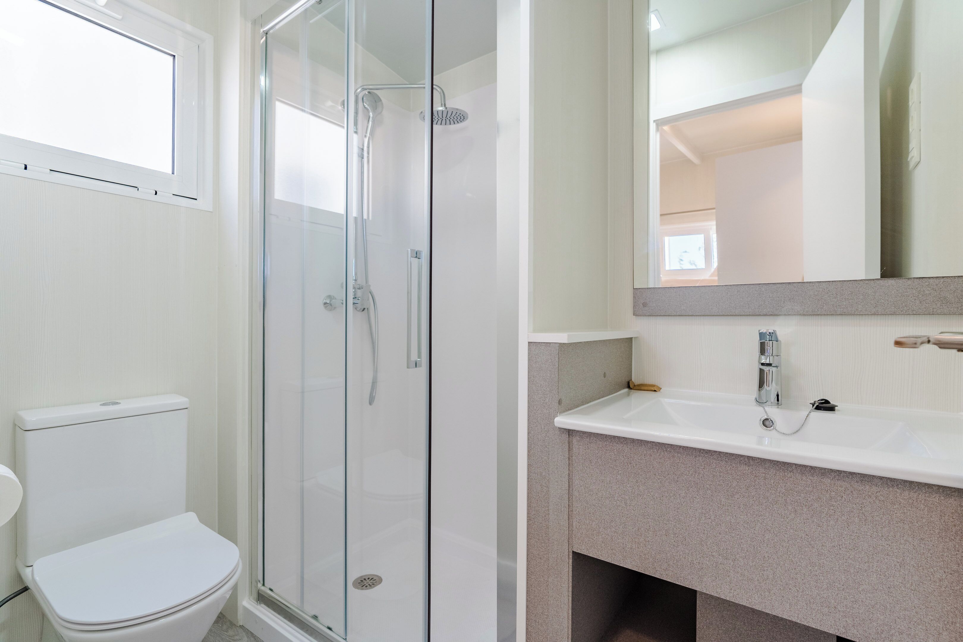Une salle de bain avec une douche à parois de verre, des toilettes blanches et un lavabo avec un miroir au-dessus.