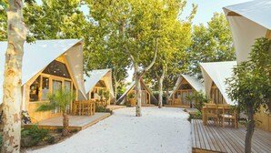 Una serie de tiendas triangulares con terrazas de madera y zonas de estar, rodeadas de árboles y suelo arenoso.