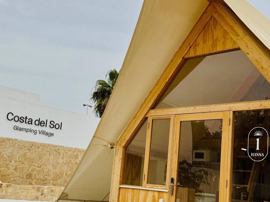 Eine Holzhütte mit einer großen Glastür und einem geneigten Dach, gelegen im Costa del Sol Glamping Village.