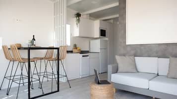 A modern kitchen with white cabinets, a dining area with wicker chairs, and a grey sofa with patterned cushions.