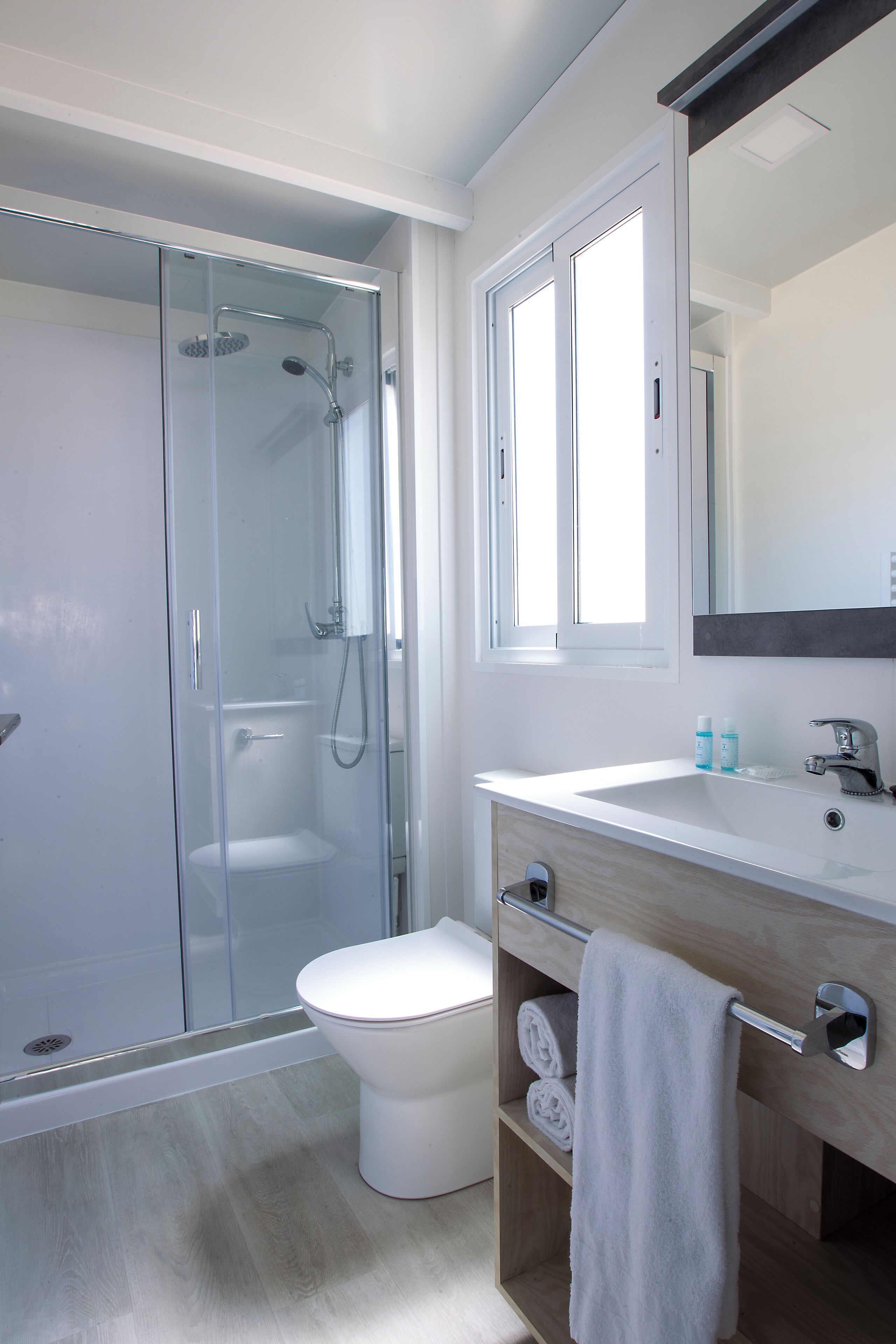 Une salle de bain moderne avec une douche à parois de verre, des toilettes blanches et un meuble-lavabo en bois avec un miroir.