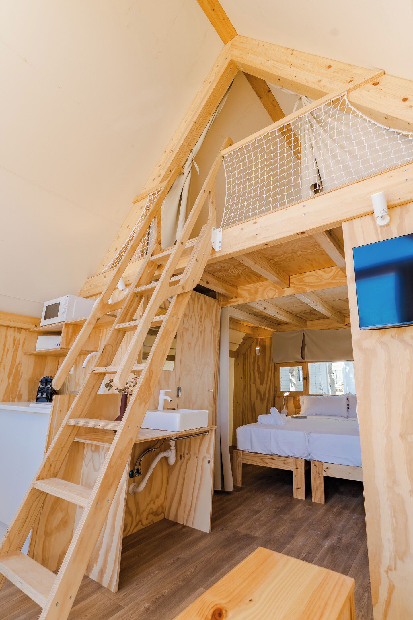 Un interior de madera con una cama alta, una escalera, un microondas y una mesita.