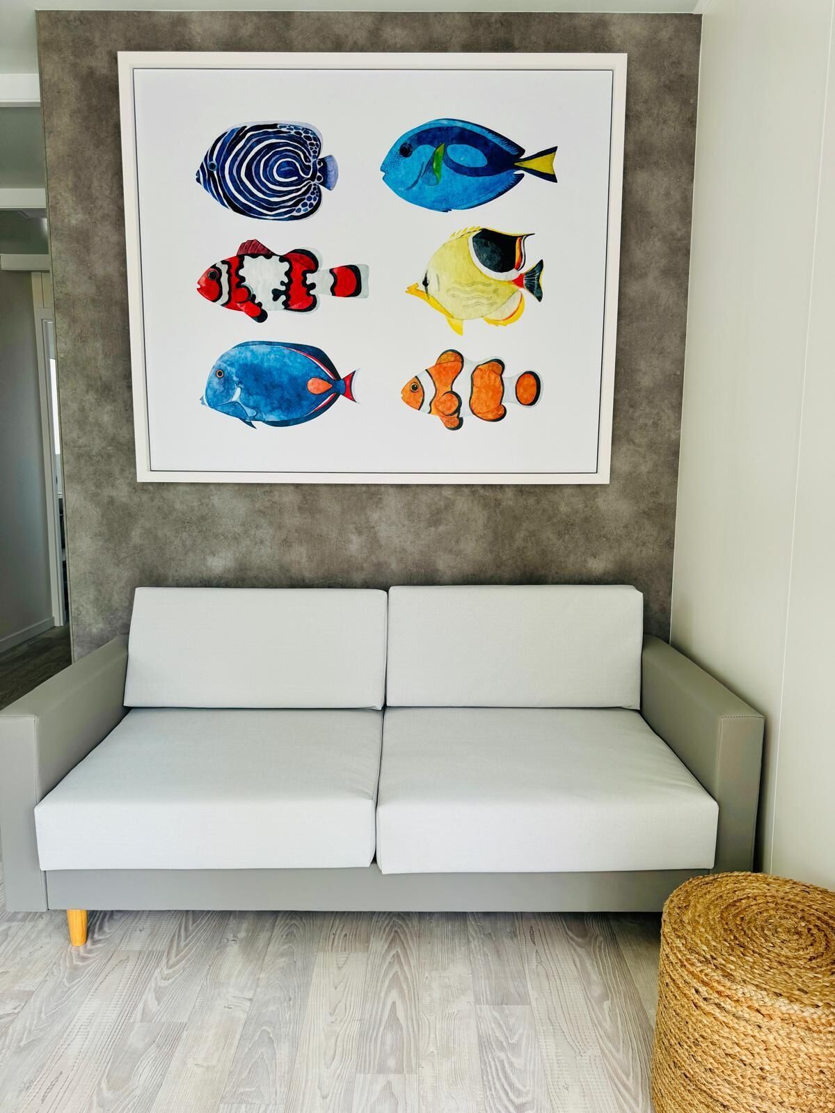 Un salon moderne avec un canapé blanc, un tableau représentant des poissons encadré au mur et un panier en osier posé sur le sol.