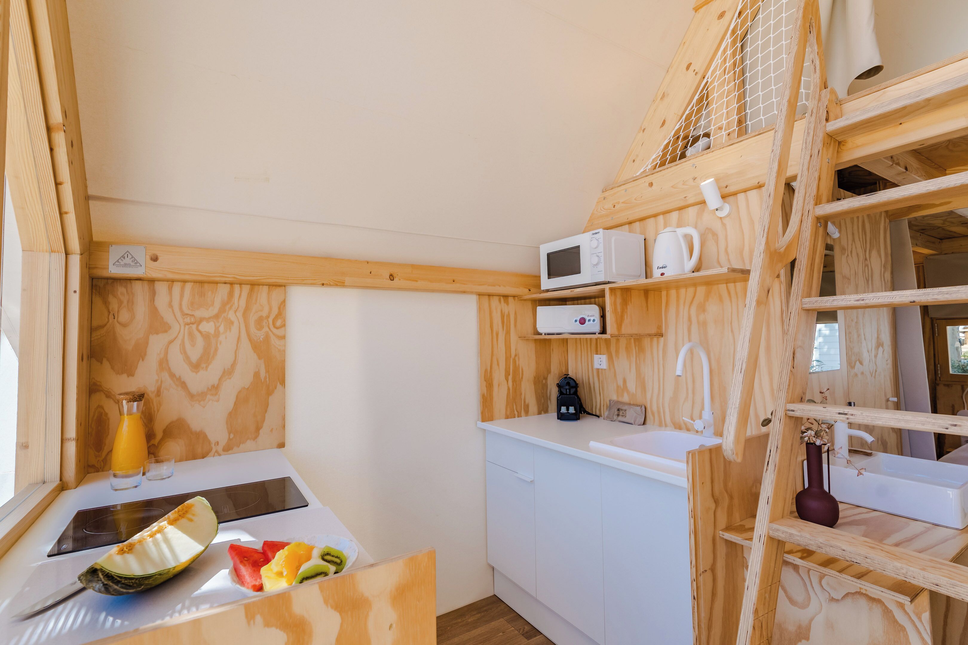 A compact kitchen with wooden cabinetry, a microwave, a kettle, and a sink.