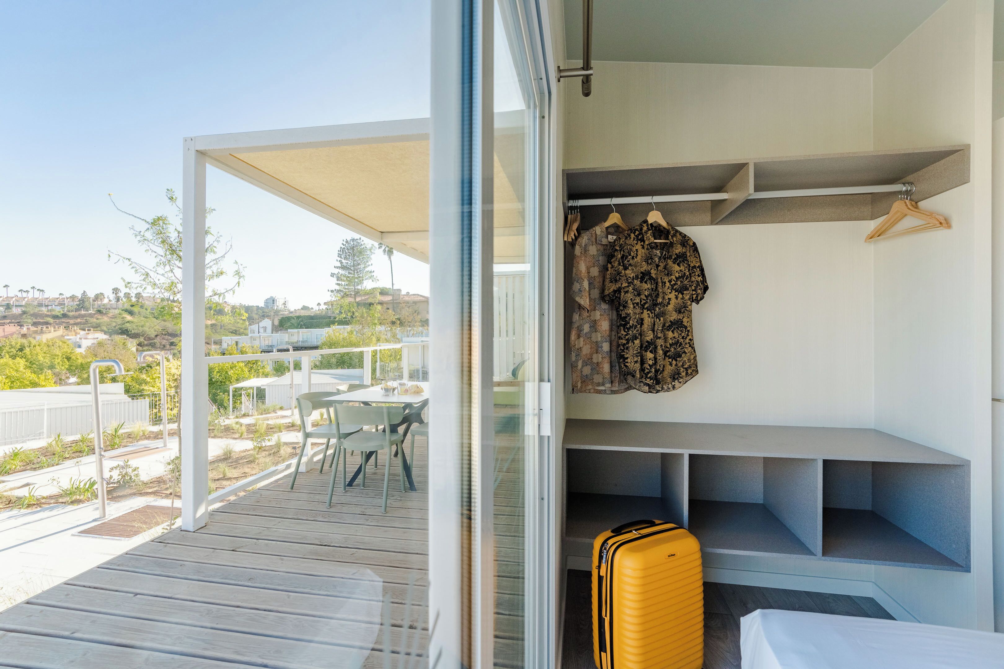 Un balcón con vistas a una zona residencial, una mesa con sillas y un perchero con ropa.