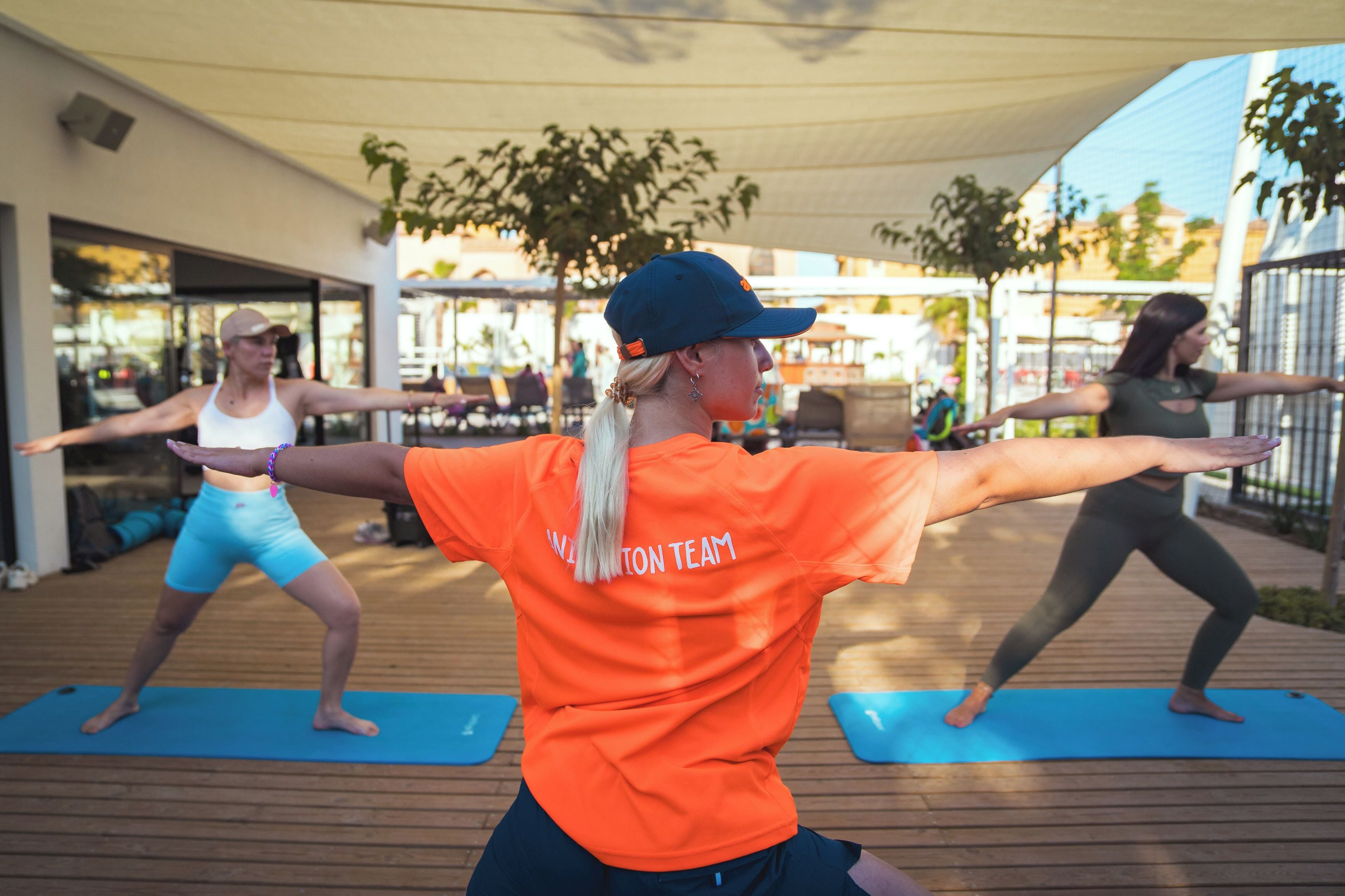 Zwei Personen führen eine Yoga-Pose im Freien auf blauen Matten aus.