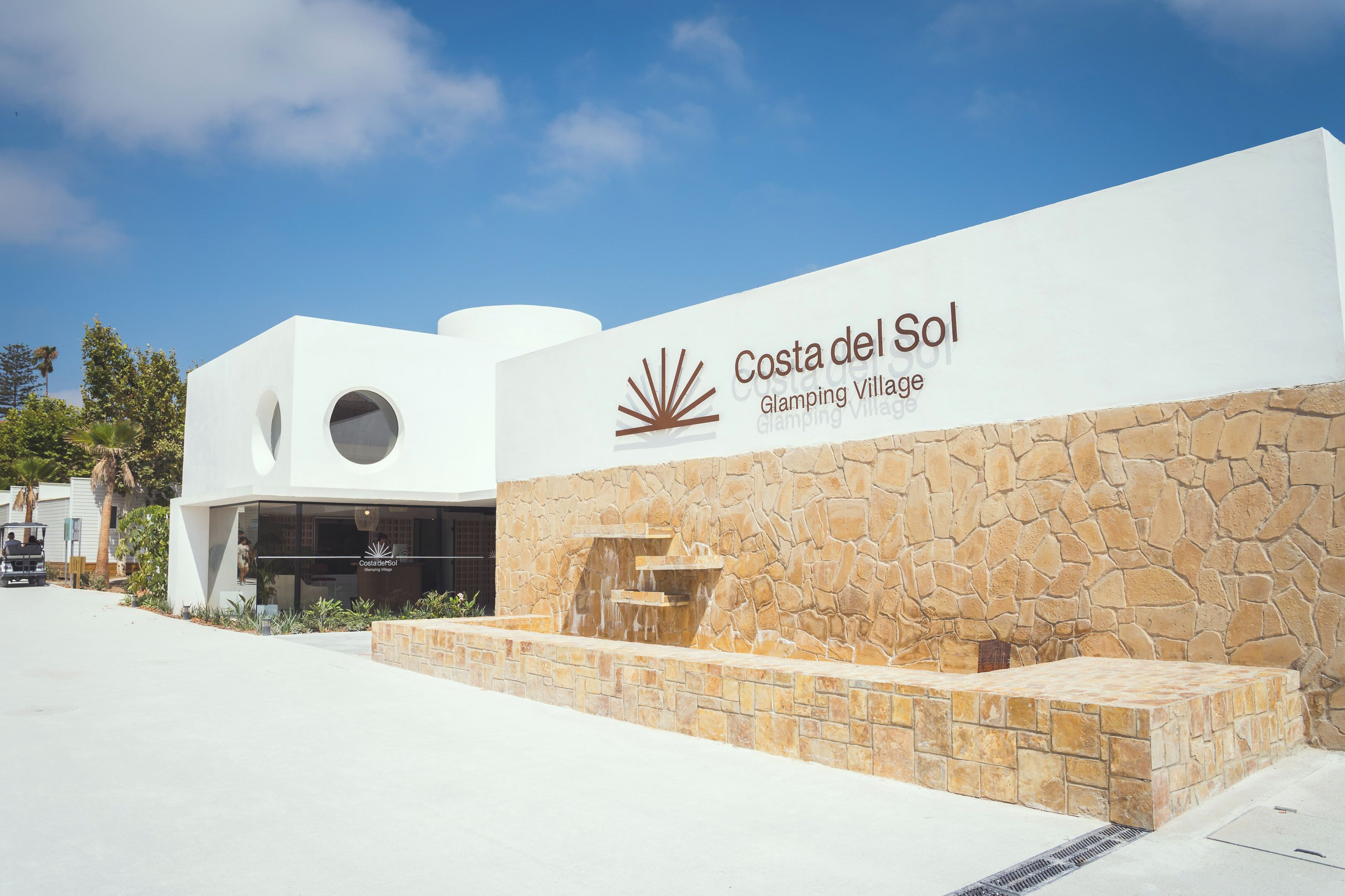 A modern building with a stone facade and a sign reading "Costa del Sol Glamping Village."