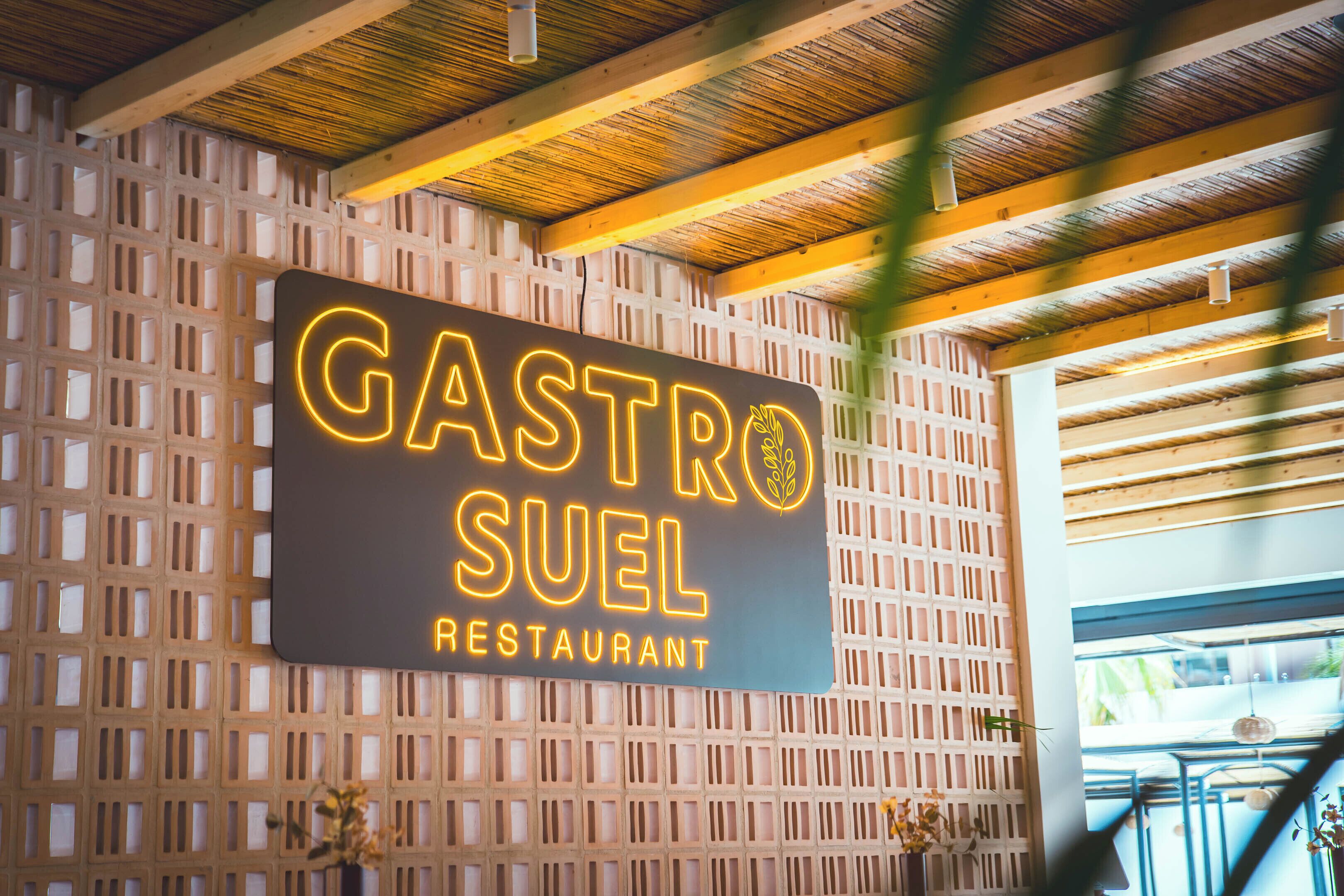 Un letrero de restaurante con el nombre 'Gastro Suel' en una pared de celosía de madera.