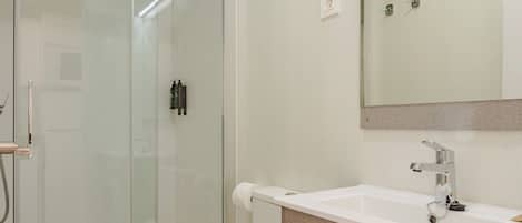 A modern bathroom with a glass-enclosed shower, a white toilet, and a beige vanity with a mirror.